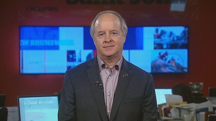 A man is sitting on a television set for an interview with the news.