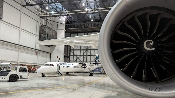 The engine of a large carrier parked in a hangar. A Q400 Bombardier is parked, but at the bottom of the hangar.