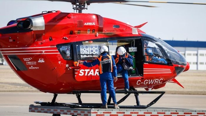 A red helicopter with a person on board and another outside.