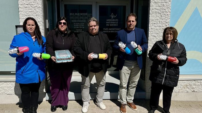 Five people stand in front of the office of a deputy by holding giant pills and a cake in their hands.