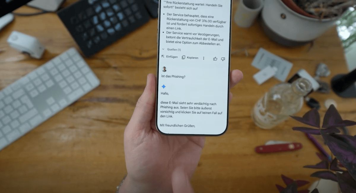 Hand holding holding a smartphone with a suspicious email displayed on the screen, surrounded by office objects such as a keyboard, a plant and a bottle. Hand holding holding a smartphone with a suspicious email displayed on the screen, surrounded by office objects such as a keyboard, a plant and a bottle.