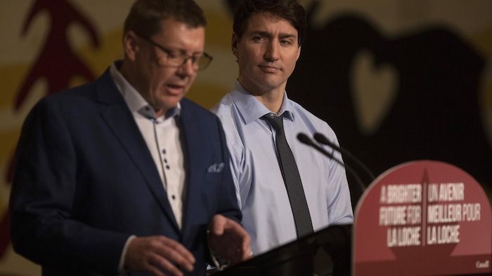 Scott Moe making a speech. In the background, Justin Trudeau looks at him.