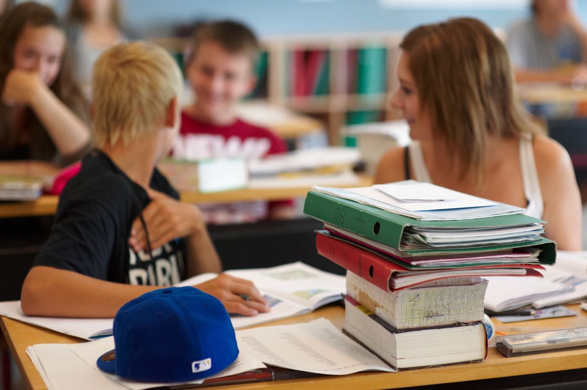 Students in class discuss a pile of books and school bags. Students in class discuss a pile of books and school bags.