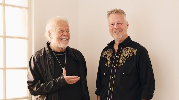 The father and the son, two musicians, smile next to each other.
