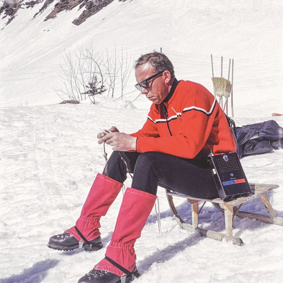Hubert Fröhlich on break on the snow, dressed in a red outfit, with mountains in the background. Hubert Fröhlich on break on the snow, dressed in a red outfit, with mountains in the background.