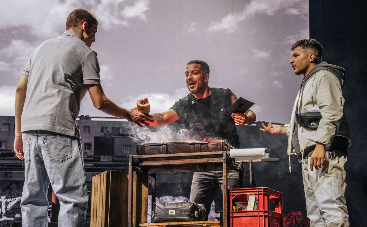 Three men interact around a barbecue during a theatrical performance, with an urban city background in the background. Three men interact around a barbecue during a theatrical performance, with an urban city background in the background.