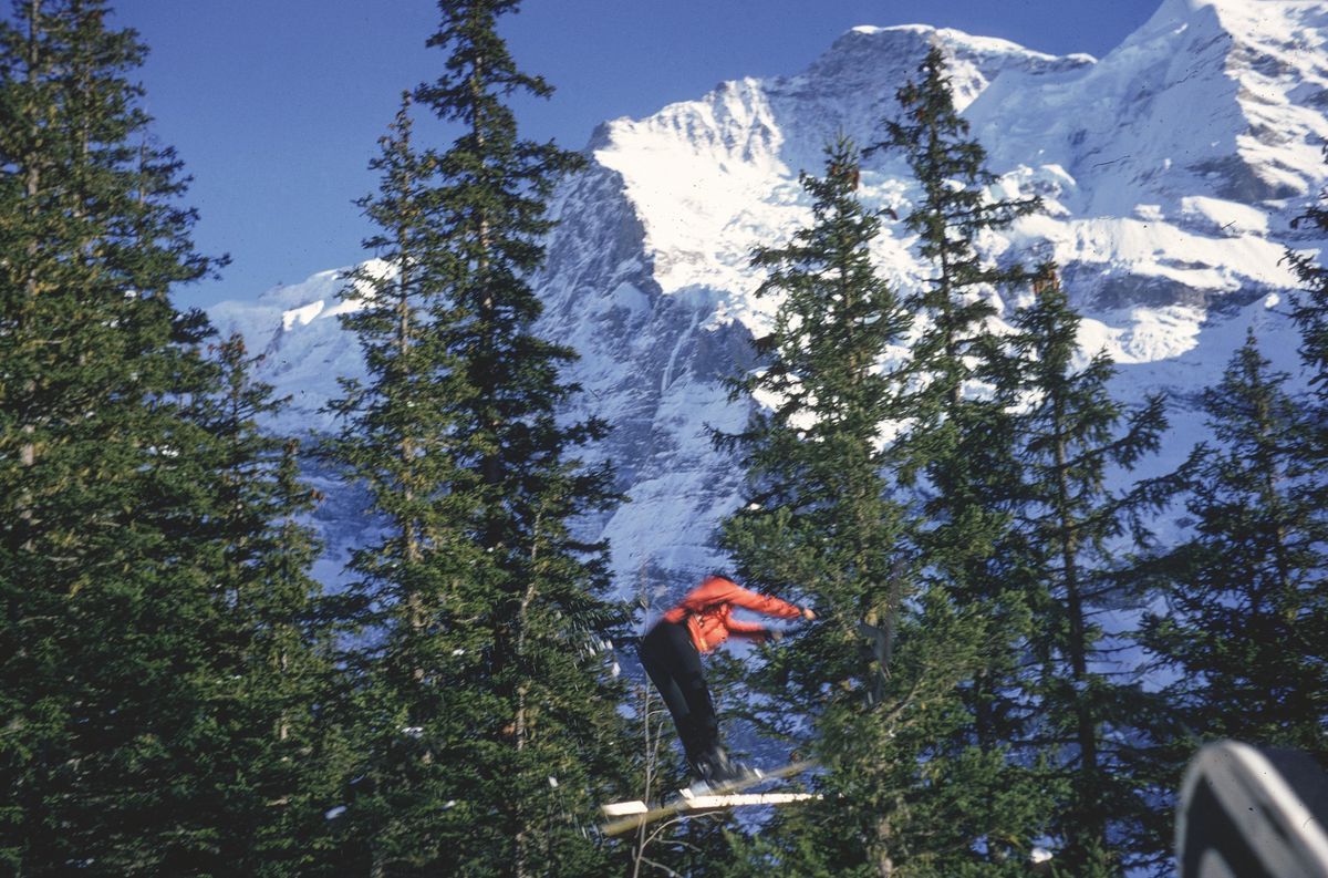 Skier in full jump among fir trees, with snowy mountain in the background. Skier in full jump among fir trees, with snowy mountain in the background.
