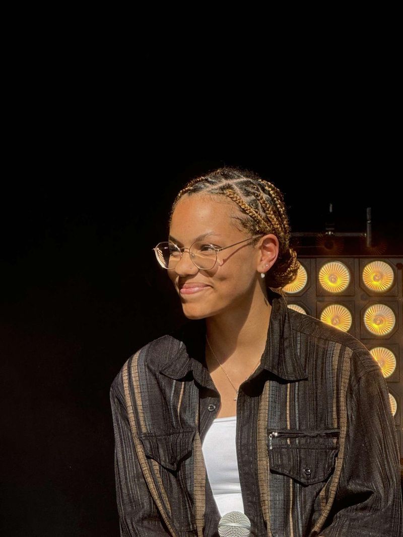 The singer Lenda smiles on stage, holding a microphone, with lighting of projectors in the background. The singer Lenda smiles on stage, holding a microphone, with lighting of projectors in the background.
