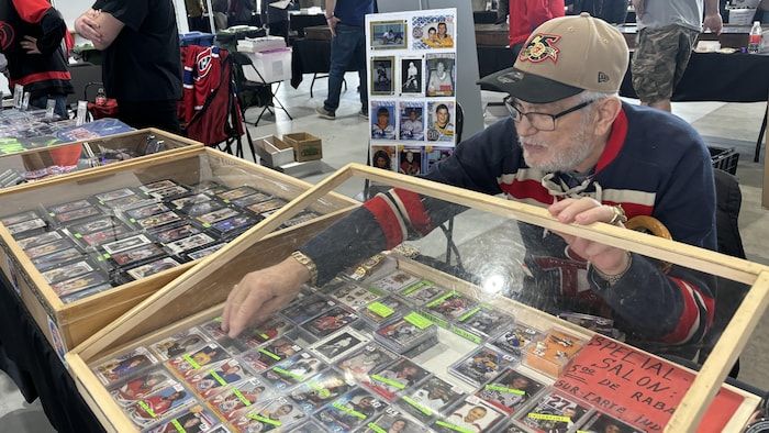 A seated man who opens a showcase in front of him to get a hockey card.