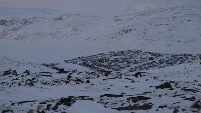 Plunging view of an arctic village, on the edge of an icy bay.