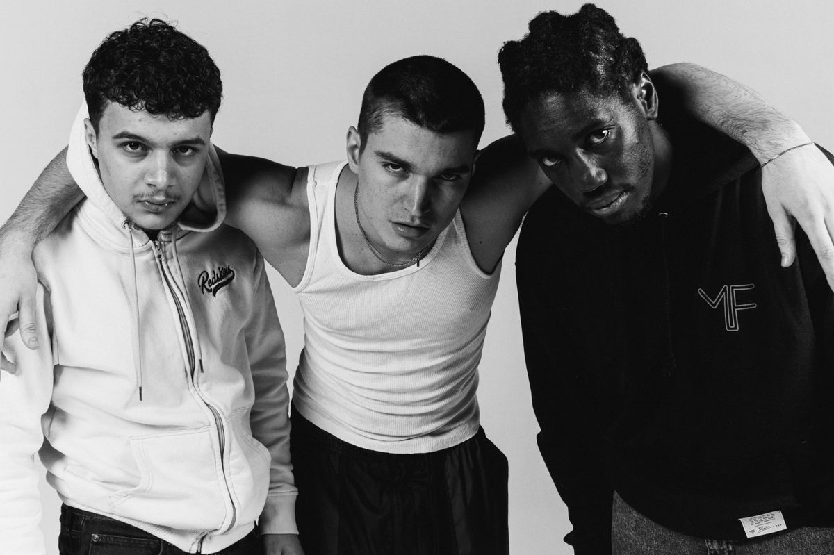 Three men posing together, two in hooded sweatshirts and one in tank top, on a white background. Three men posing together, two in hooded sweatshirts and one in tank top, on a white background.