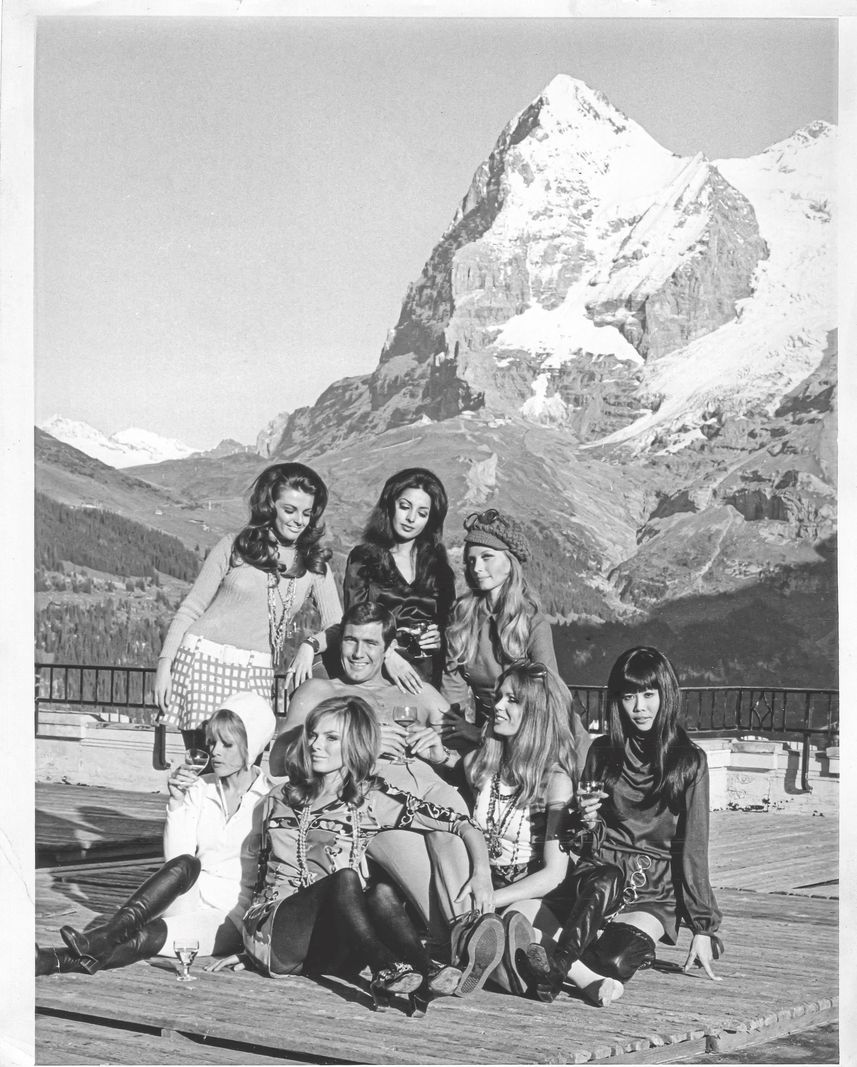 Lazenby surrounded by seven bond girls in front of the Palace hotel in Mürren, with a view of Mont Eiger in the background. Lazenby surrounded by seven bond girls in front of the Palace hotel in Mürren, with a view of Mont Eiger in the background.