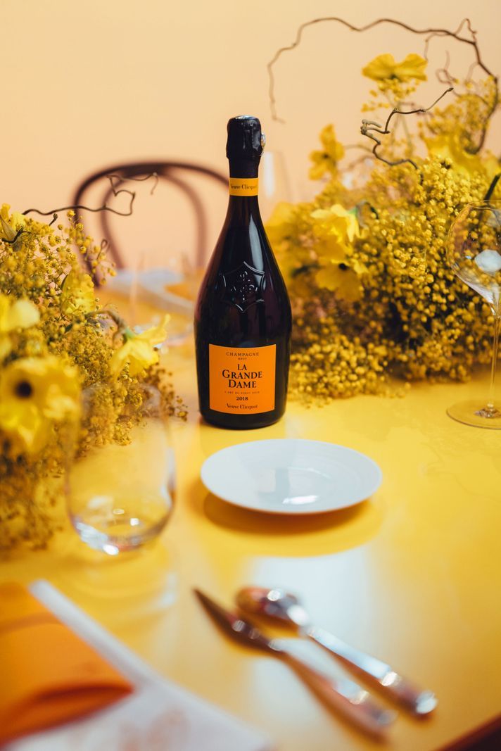Bottle of champagne La Grande Dame on a table decorated with yellow flowers, glasses and cutlery. Bottle of champagne La Grande Dame on a table decorated with yellow flowers, glasses and cutlery.