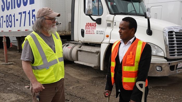 Jonas Hila, founder of the Jonas Driving School driving school, chats with a man in front of a trailer truck from his school.