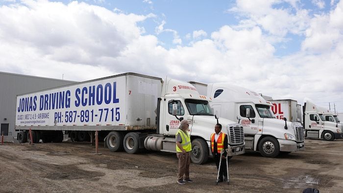 Jonas Hila, founder of the Jonas Driving School driving school, chatting with an employee in front of trucks from his driving school.