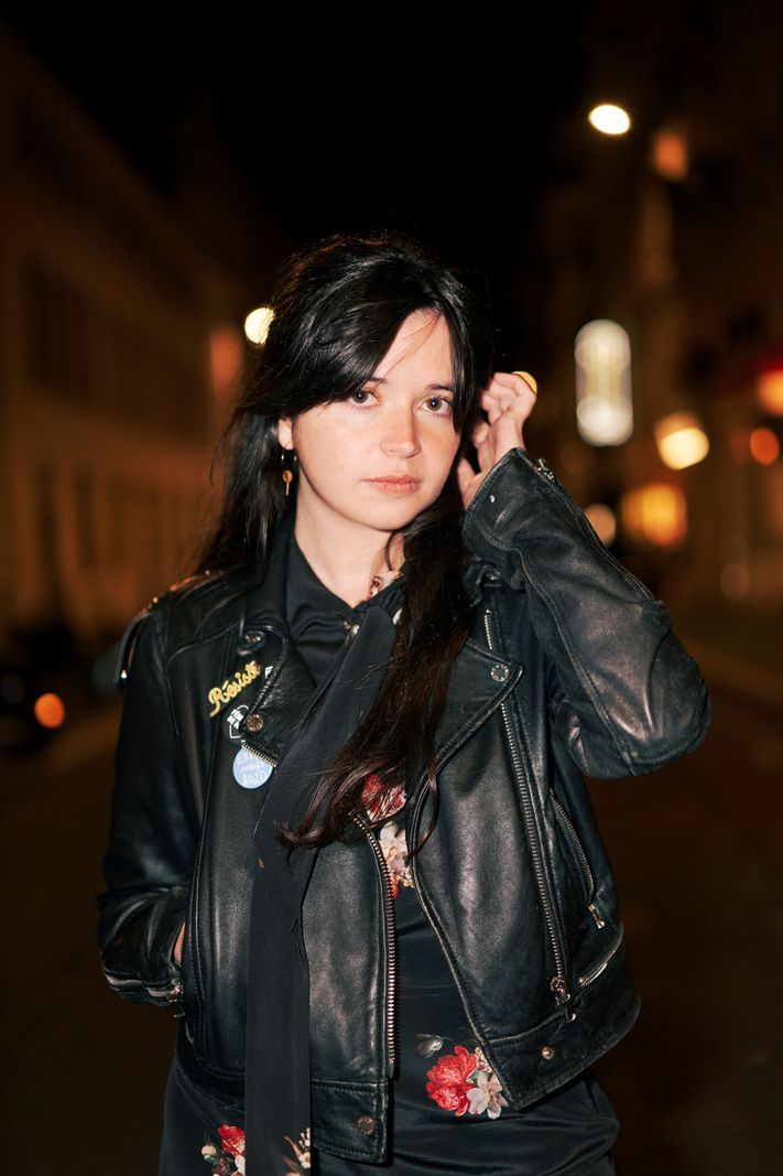 Woman in a black leather jacket, standing in a street lit at night, with buildings in the background. Woman in a black leather jacket, standing in a street lit at night, with buildings in the background.