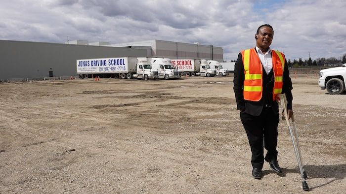 Jonas Hila, standing, two crutches in hand, poses in front of his school trailers.