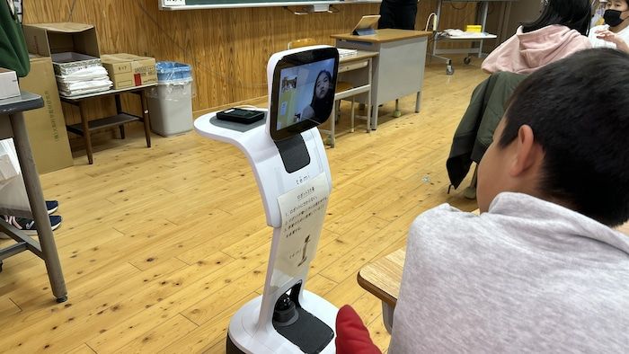 A boy looks at a robot whose head is a screen on which the face of a young girl appears.